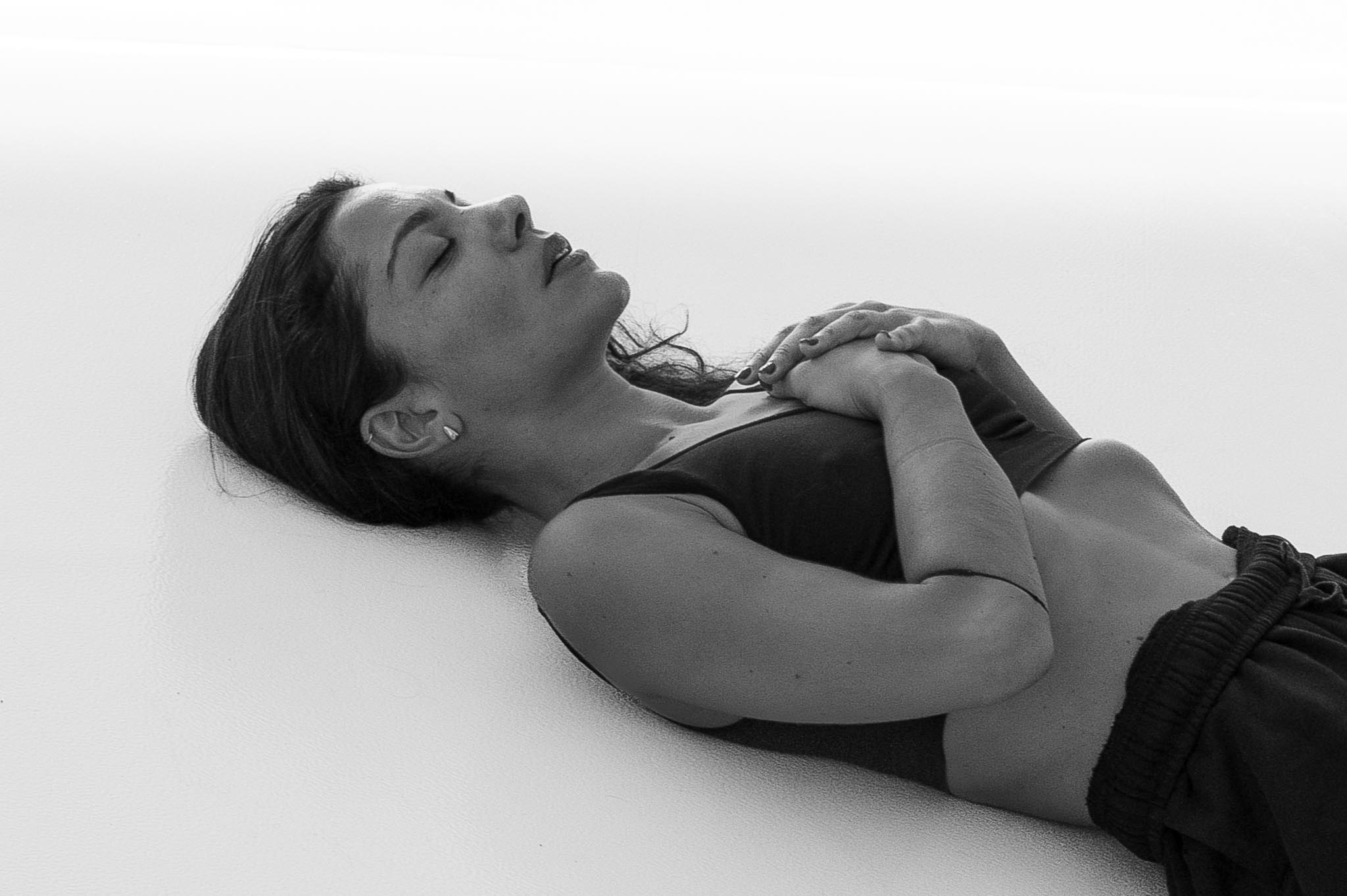 Vilelmini lying on the floor with hands on her chest, eyes closed, resting after movement.