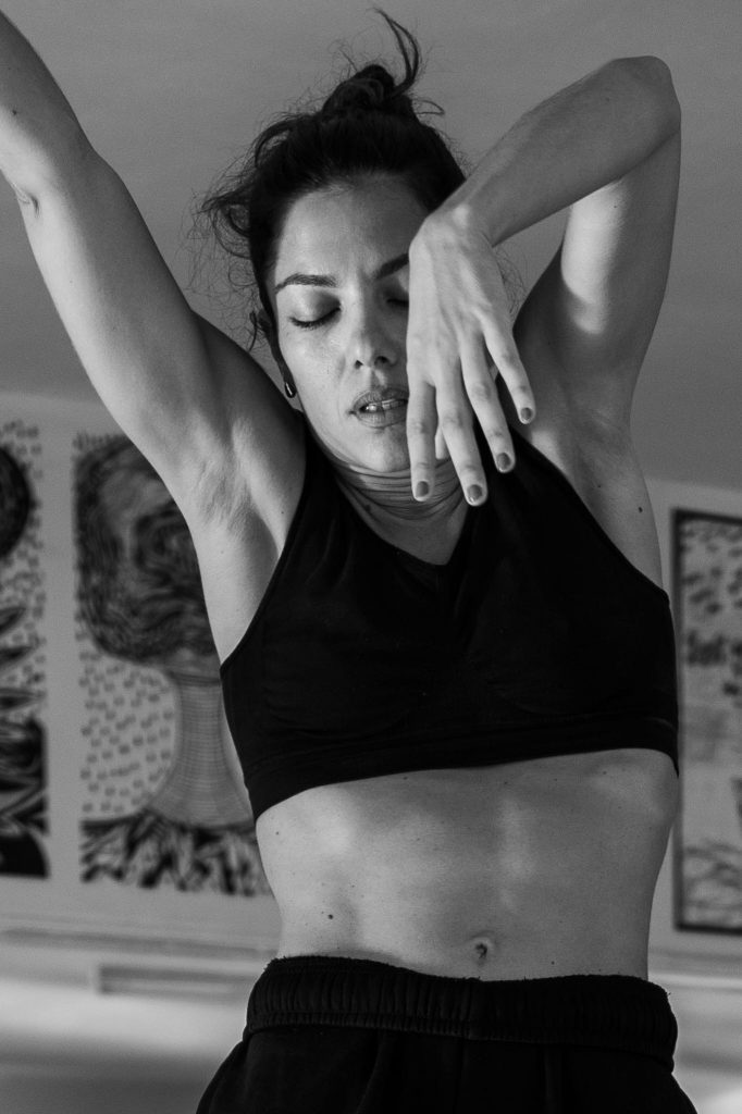 Vilelmini in an expressive dance moment, hands framing her face, eyes closed in concentration.